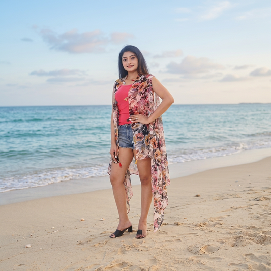 Pink & Green Floral Sleeveless Shrug with Tassels worn over a pink top and denim shorts on a beach at sunset